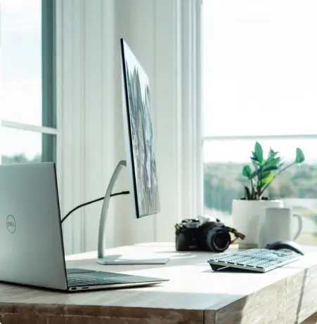 Mesa com laptop, monitor externo, câmera e planta.